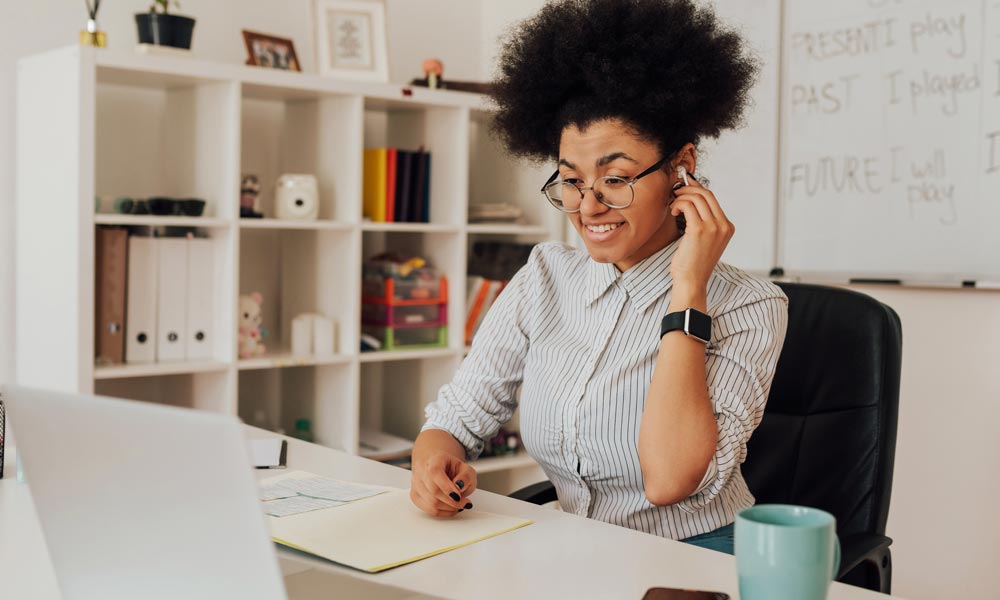 Background image of a teacher at her home desk looking at a laptop screen